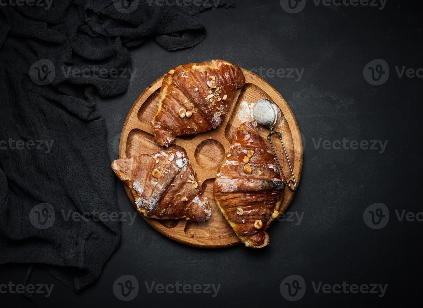 croissants horneados en una tabla de madera negra espolvoreada con azúcar en polvo, vista superior foto