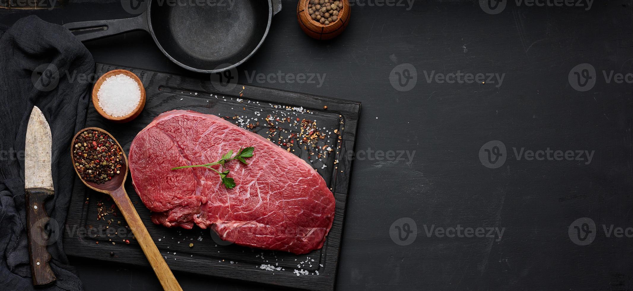 Raw beef tenderloin lies on a cutting board and spices for cooking on a black table, top view photo