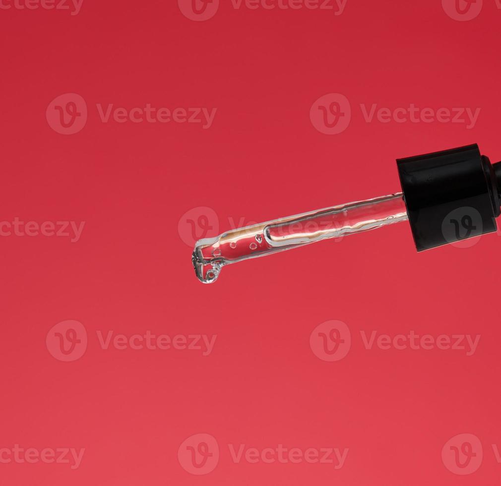 glass pipette with dripping transparent liquid on a red background photo