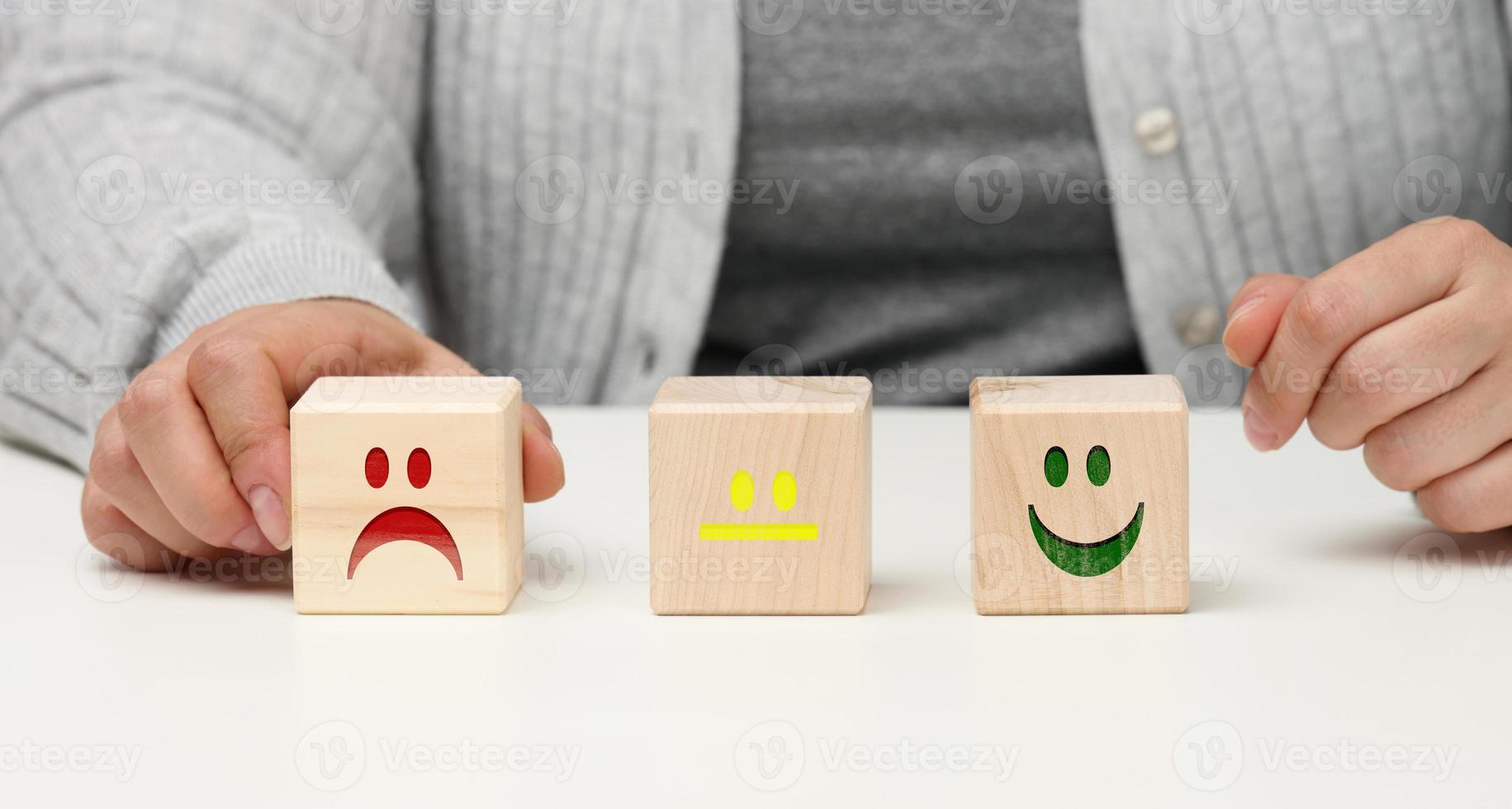 bloques de madera con diferentes emociones, desde la sonrisa hasta la tristeza y la mano de una mujer. concepto para evaluar la calidad de un producto o servicio, estado emocional, opiniones de los usuarios foto