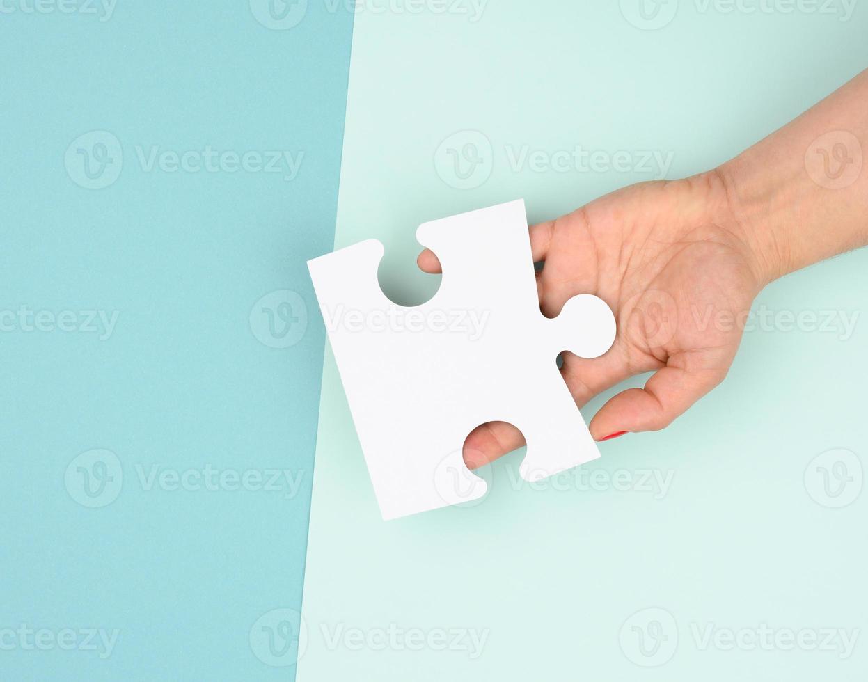 female hand holds a fragment of a white large puzzle on a blue background photo
