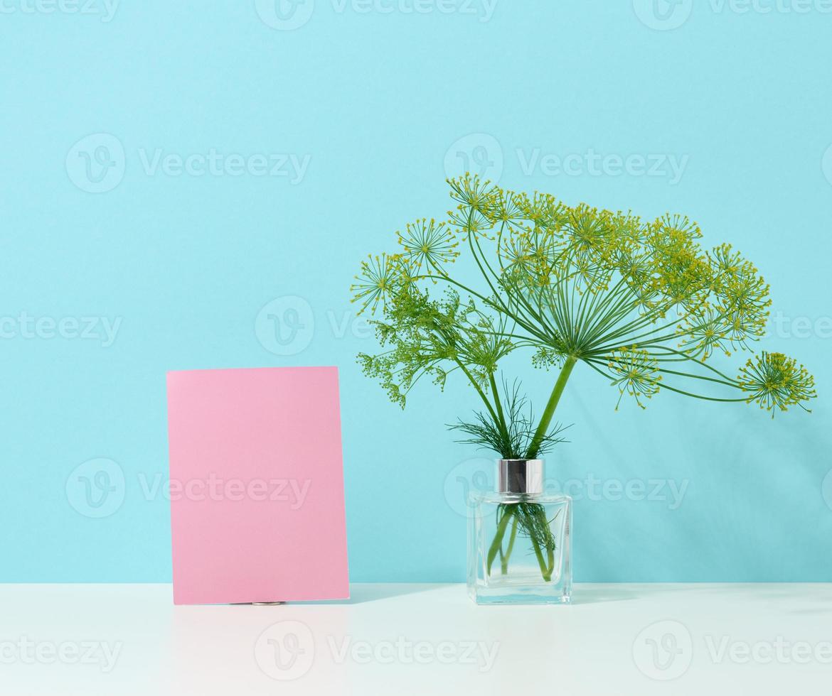 hoja de papel rosa de cartón vacía y jarrón de vidrio con un ramo de eneldo sobre una mesa blanca. minimalismo en el interior foto