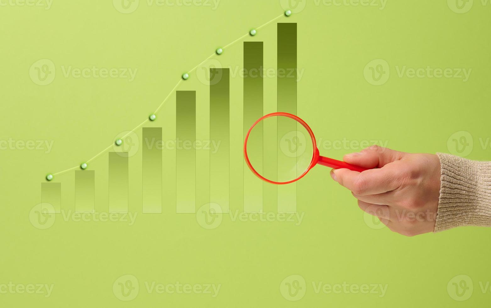 ascending bar chart and hand with red magnifying glass. Data analysis, green background photo