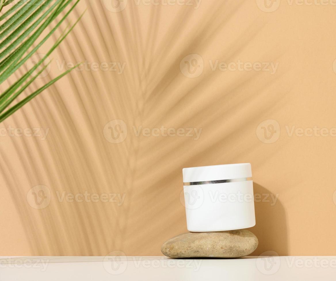 white round plastic jar for cosmetic products on a brown background. Palm leaf shadow. Blank for branding products, mock up photo