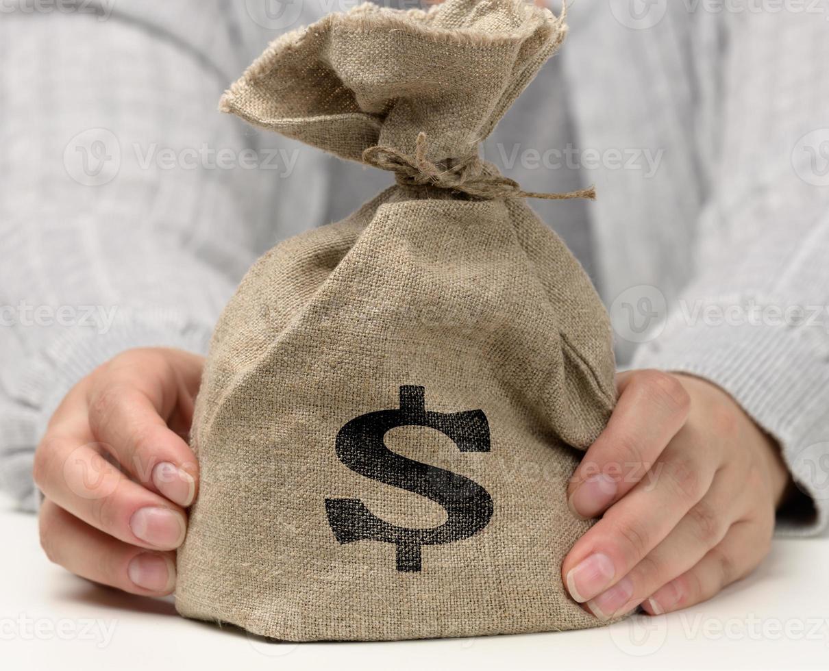 hand holds a canvas bag full of money with a US dollar icon on a white background photo