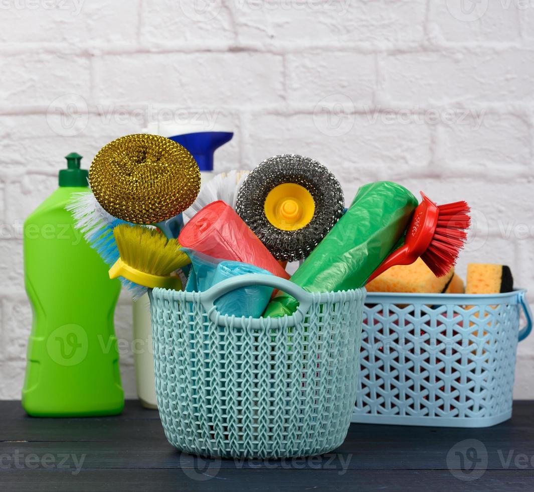 sponges, plastic brushes and bottles of detergents on a blue wooden table. Household cleaning items on white brick wall background photo
