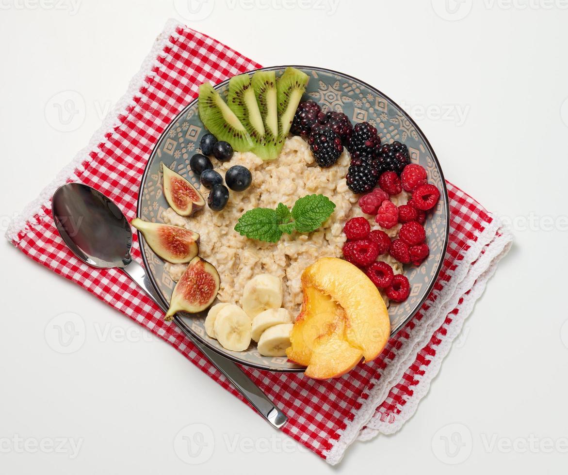 boiled oatmeal with fruit in a round plate on a white table, healthy breakfast. View from above photo