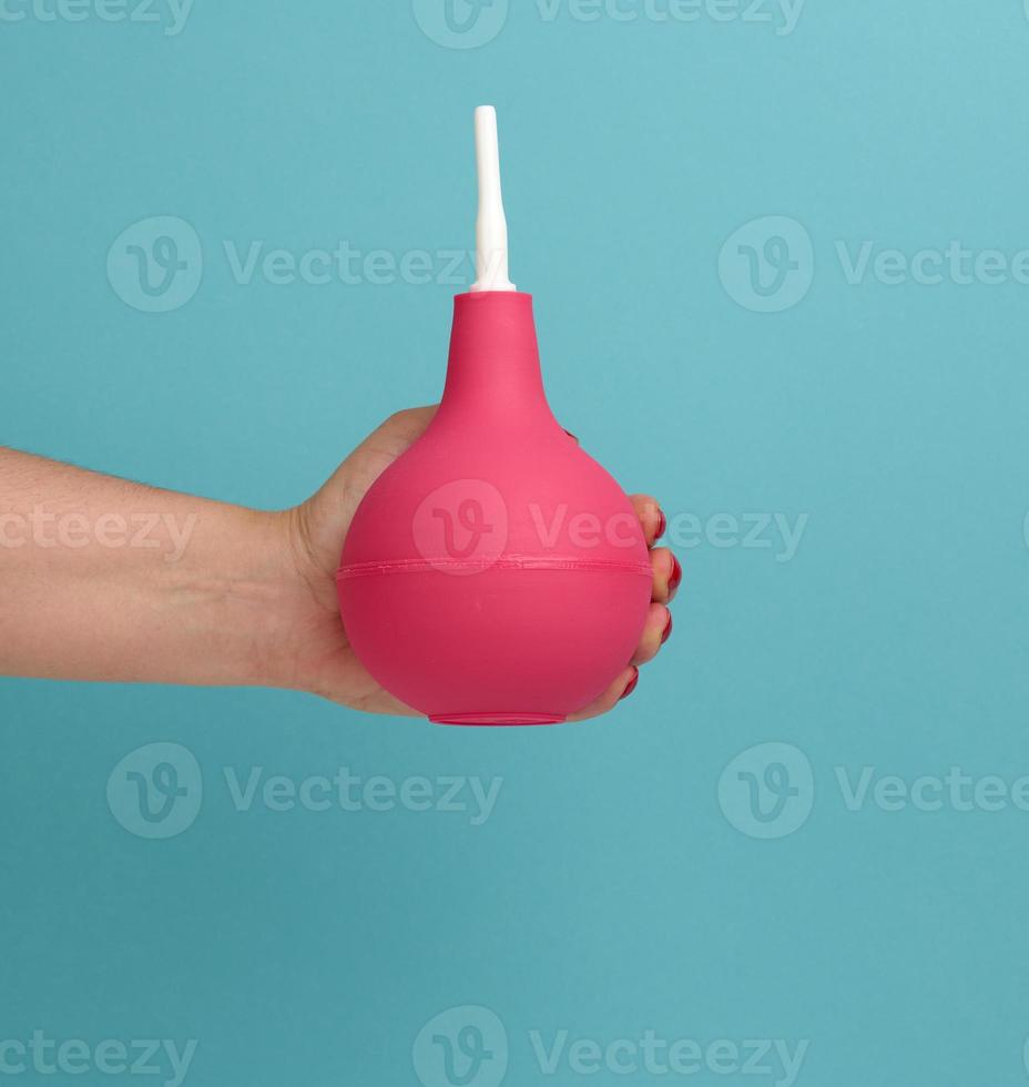 a hand in a blue medical glove holds a pink rubber enema on a blue background photo