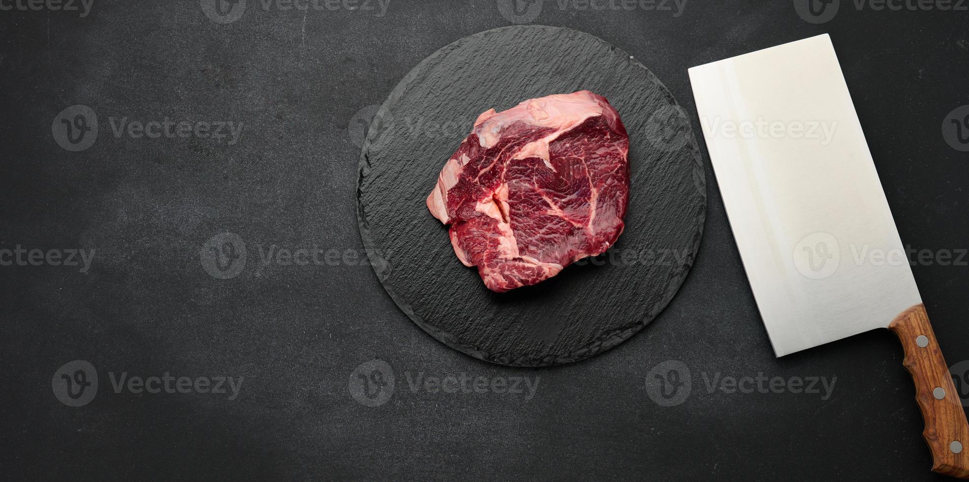round raw piece of beef meat on a black board. Ribeye for barbecue photo