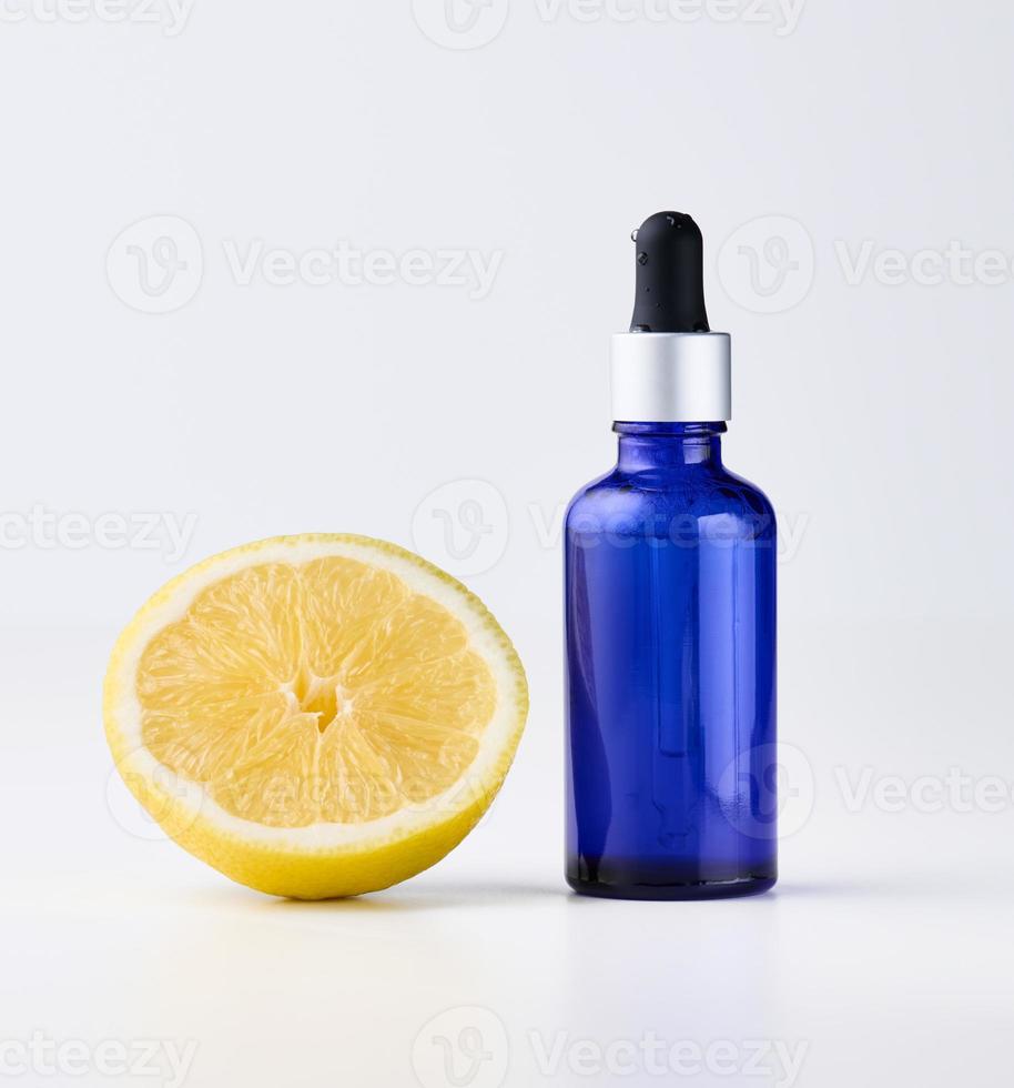 Blue glass bottle with pipette, next to it is half a lemon on a white front. photo