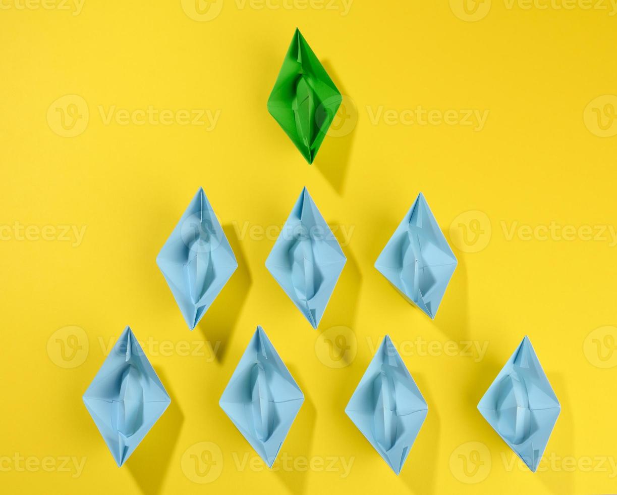 group of paper boats on a yellow background. concept of a strong leader in a team, manipulation of the masses, following new perspectives photo