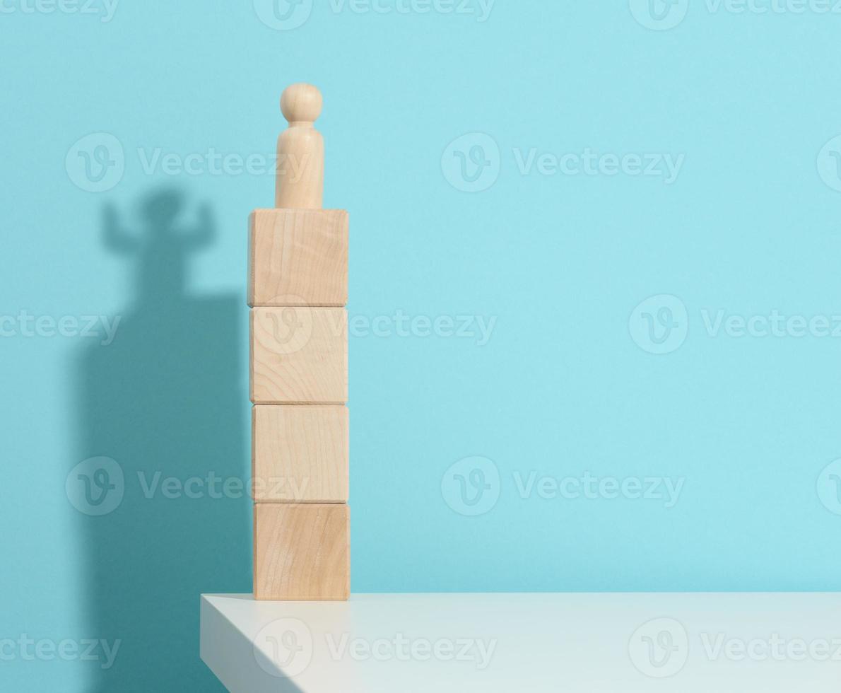 estatuilla de madera de un hombre se encuentra en lo alto de los cubos, la sombra de un fuerte y victorioso. todo el mundo es más fuerte de lo que piensa, un superhéroe. fondo azul foto