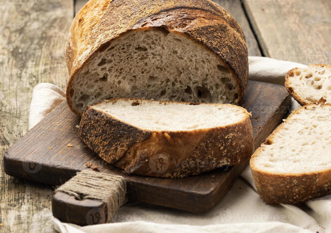 baked round bread made from white wheat board on wooden board, loaf cut into pieces photo