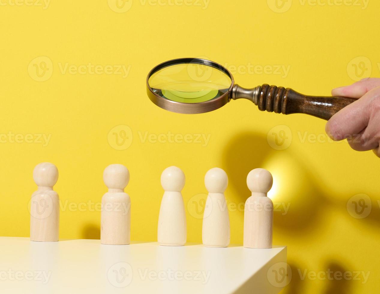 figurines of men on a white table and magnifying glass. Concept of searching for employees in the company, recruiting personnel, identifying talented and strong personaliti photo