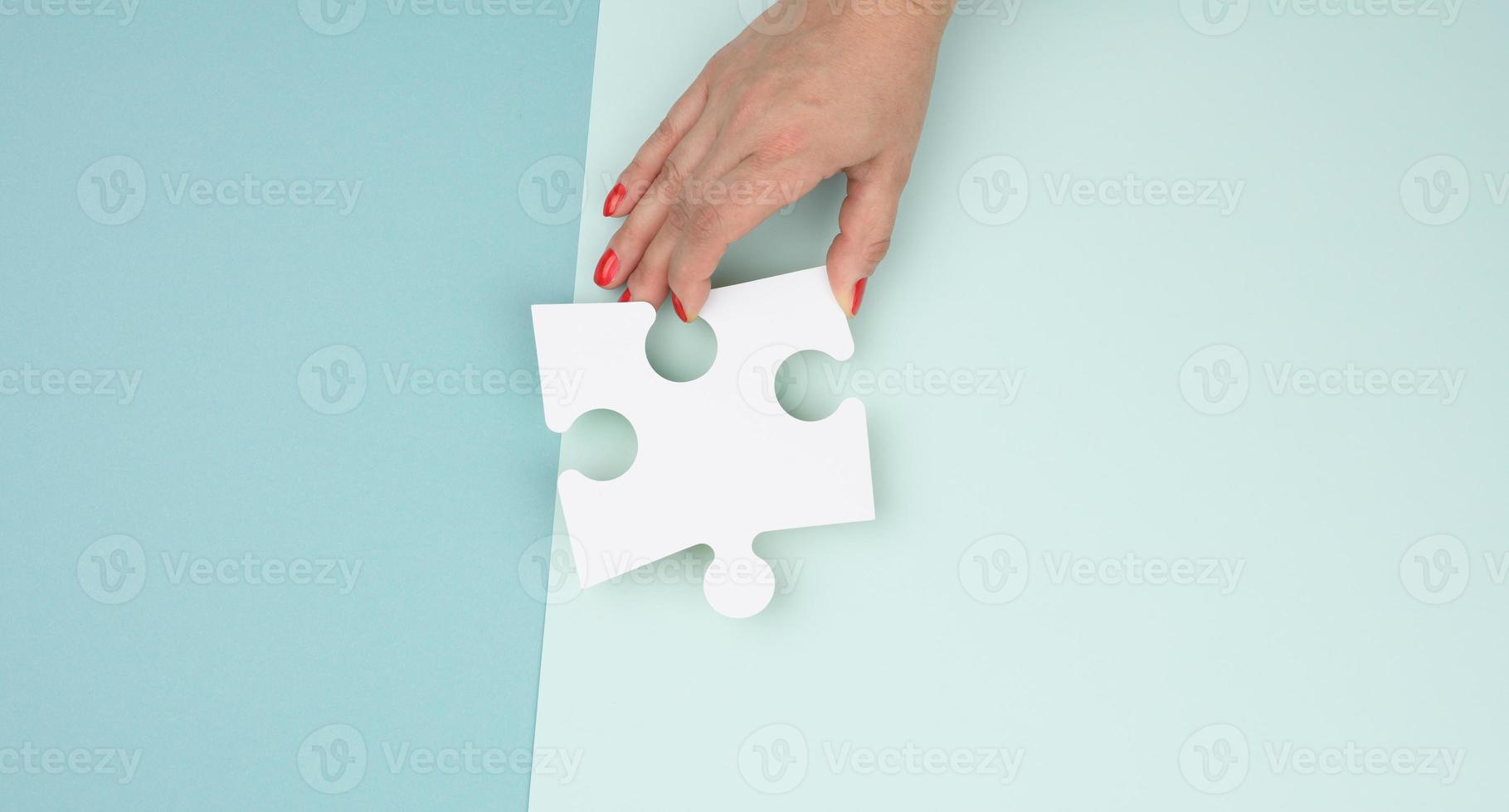 female hand holds a fragment of a white large puzzle on a blue background photo