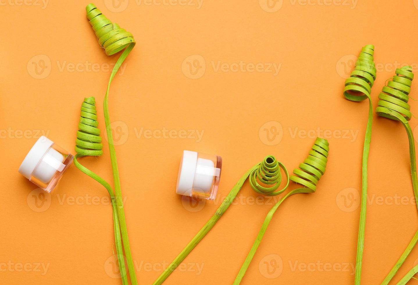 empty white glass jars with plastic lid on orange background with green decor. Packaging for cream, gel, serum, advertising and product promotion. Mock up photo