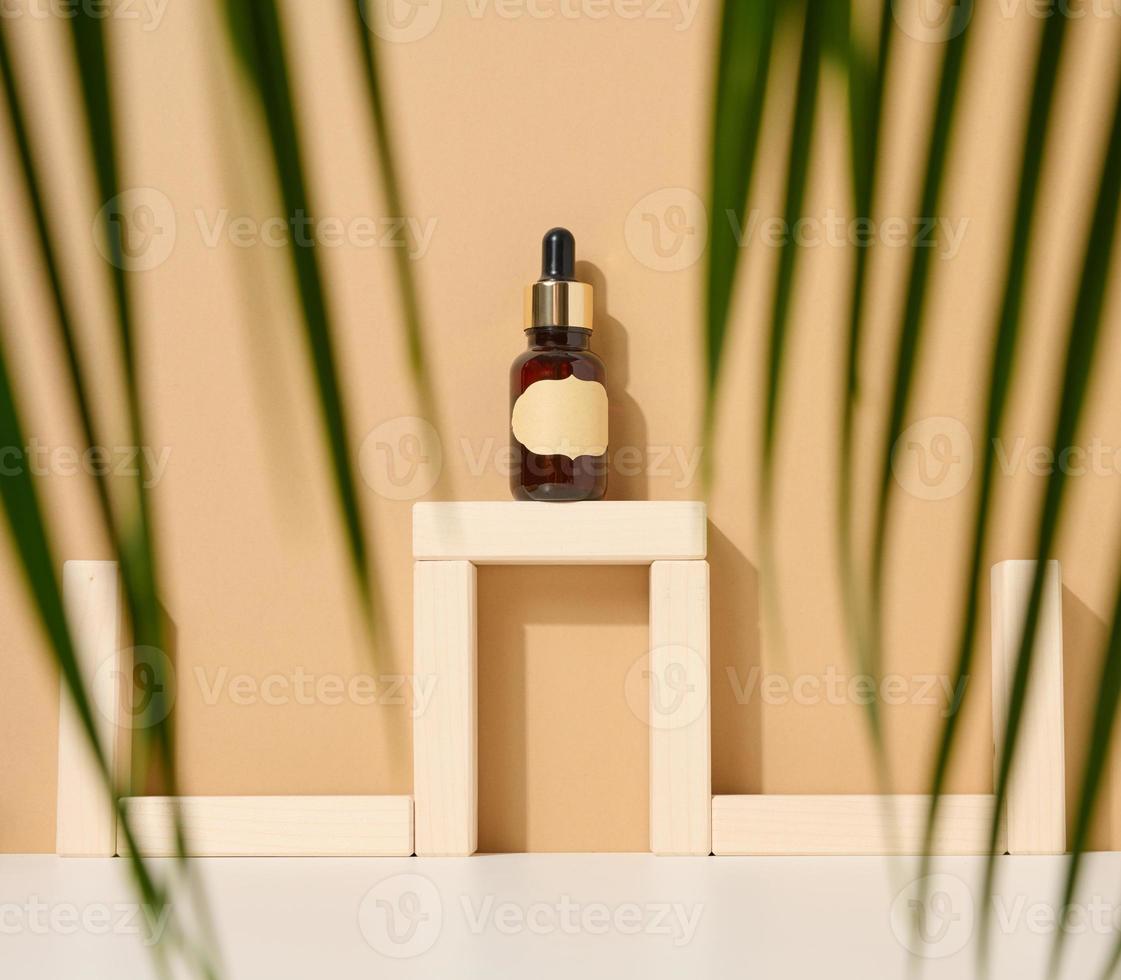 glass brown bottle with pipette and paper blank label on light brown background. Mockup skincare cosmetic product photo