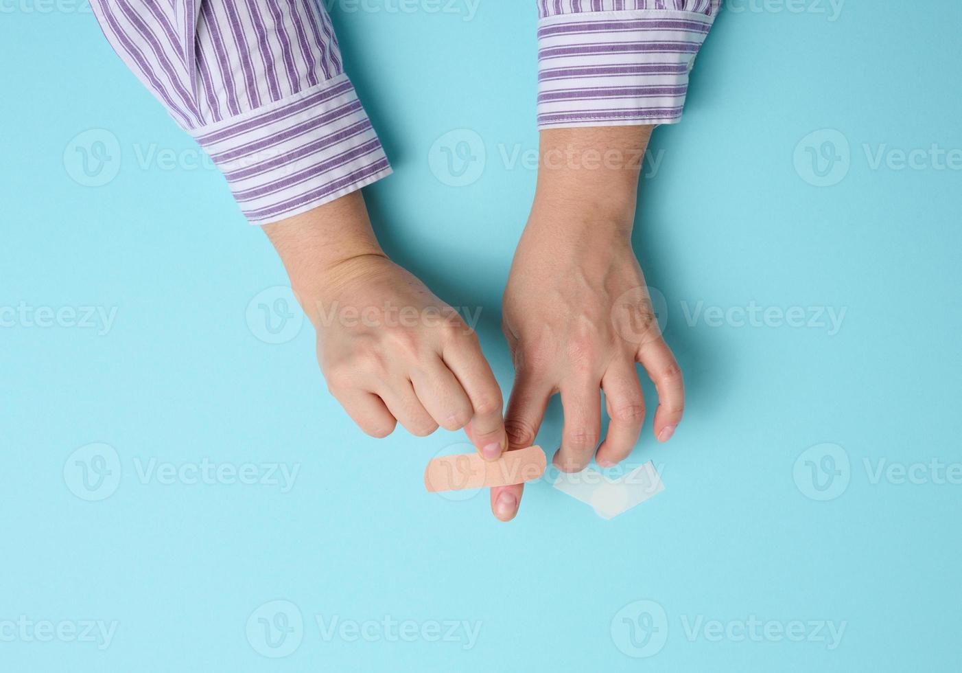 female hand and brown medical adhesive plaster for the treatment of injuries and cuts on the skin, blue background photo