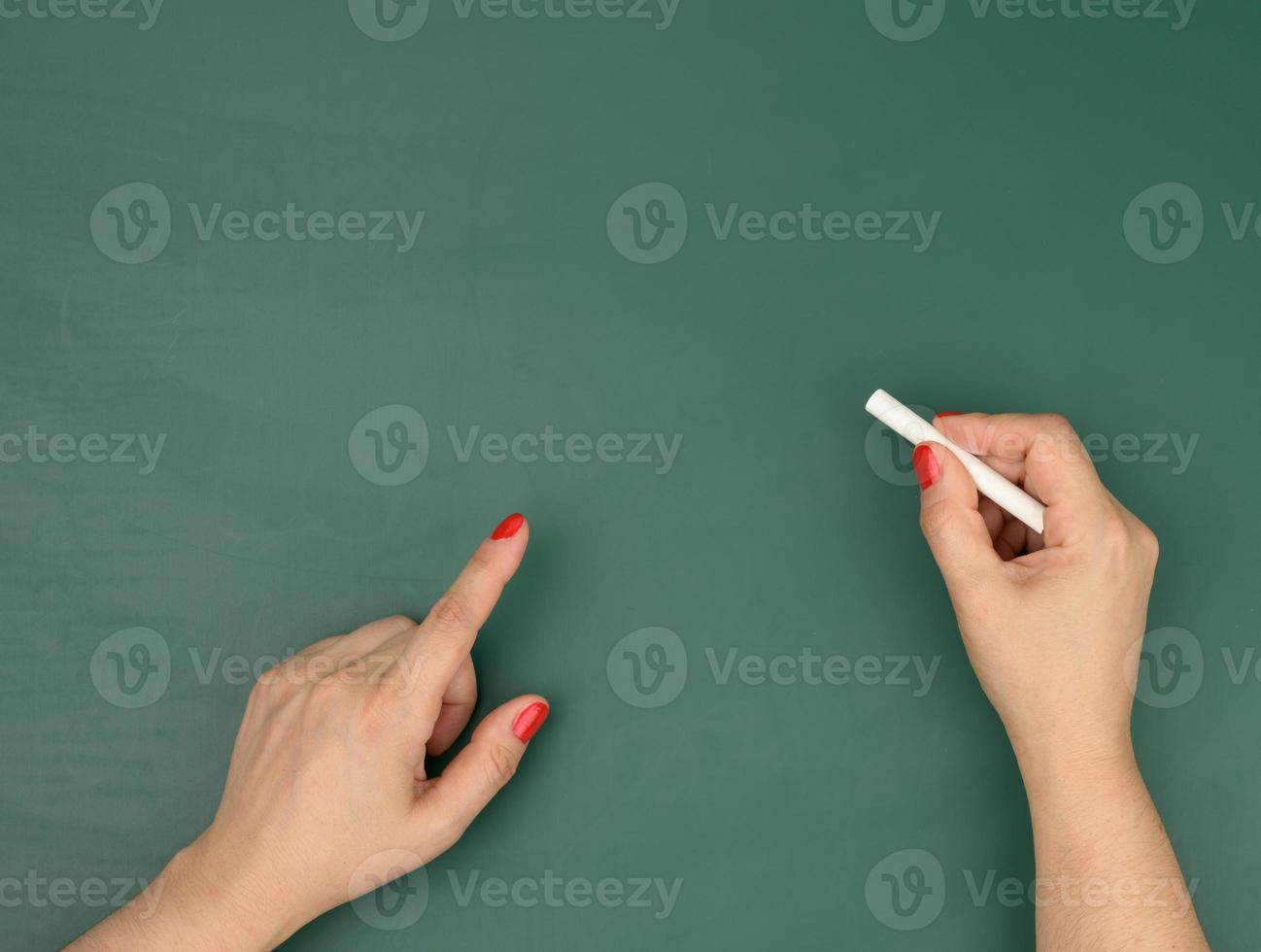 hand holds a piece of white chalk on the background of an empty green chalk board, presentation concept photo