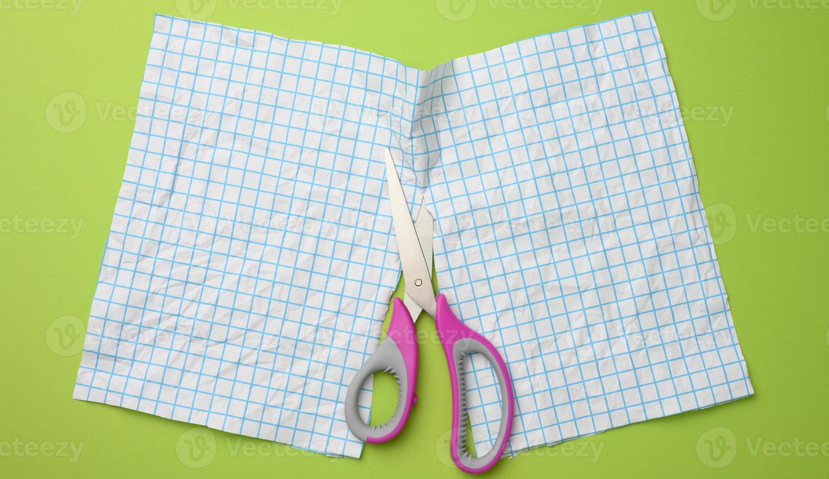 a sheet of white paper cut in half with scissors in a blue box on a green background photo