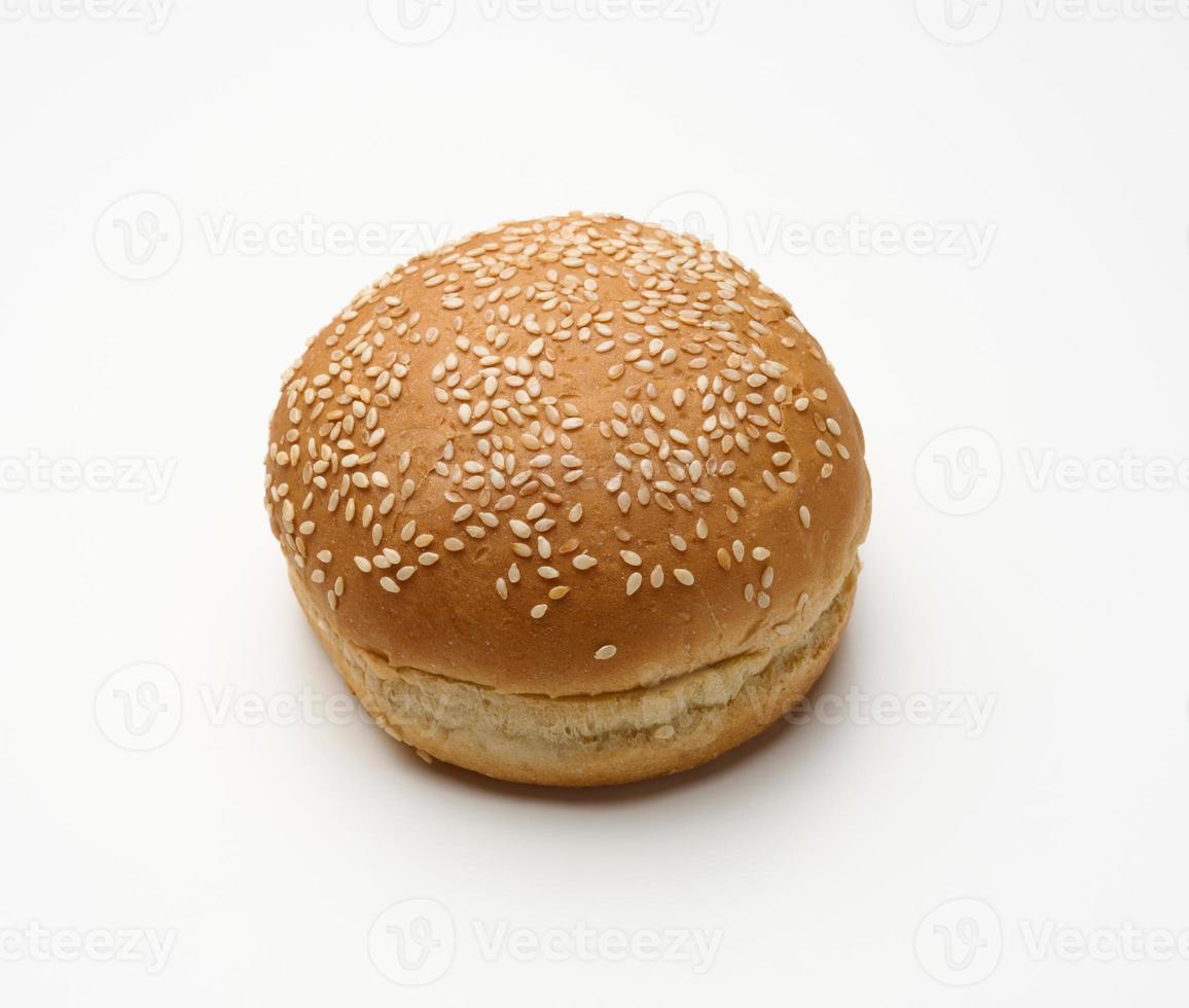 baked round fresh white wheat flour bun sprinkled with sesame seeds on a white table. Hamburger, cheeseberger and sandwich bun photo