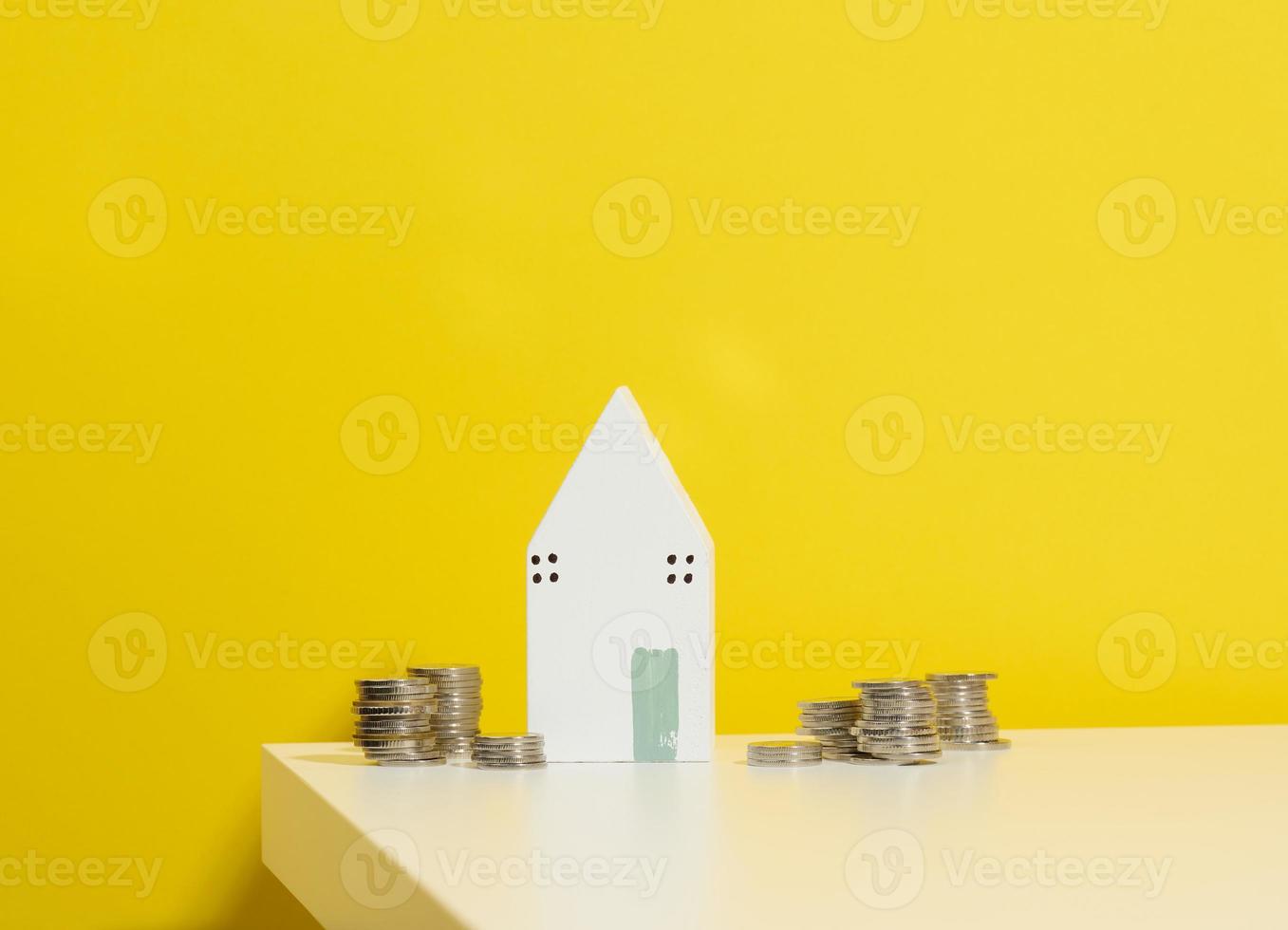 miniature wooden house and a stack of coins on a white table. Real estate purchase, mortgage concept. Rise in real estate prices, subsidies from the state photo