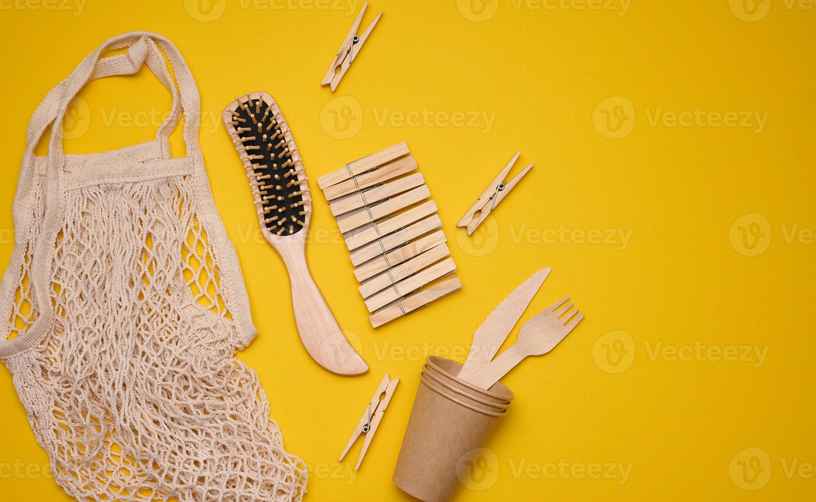 white cotton bag, paper cups and wooden forks and spoons on a yellow background. Recyclable waste, top view photo
