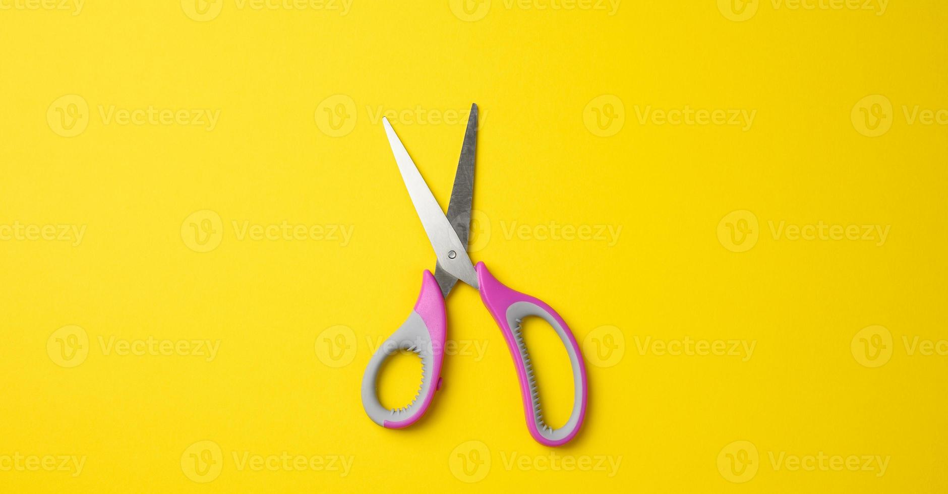 metal scissors with pink plastic handle on a yellow background photo