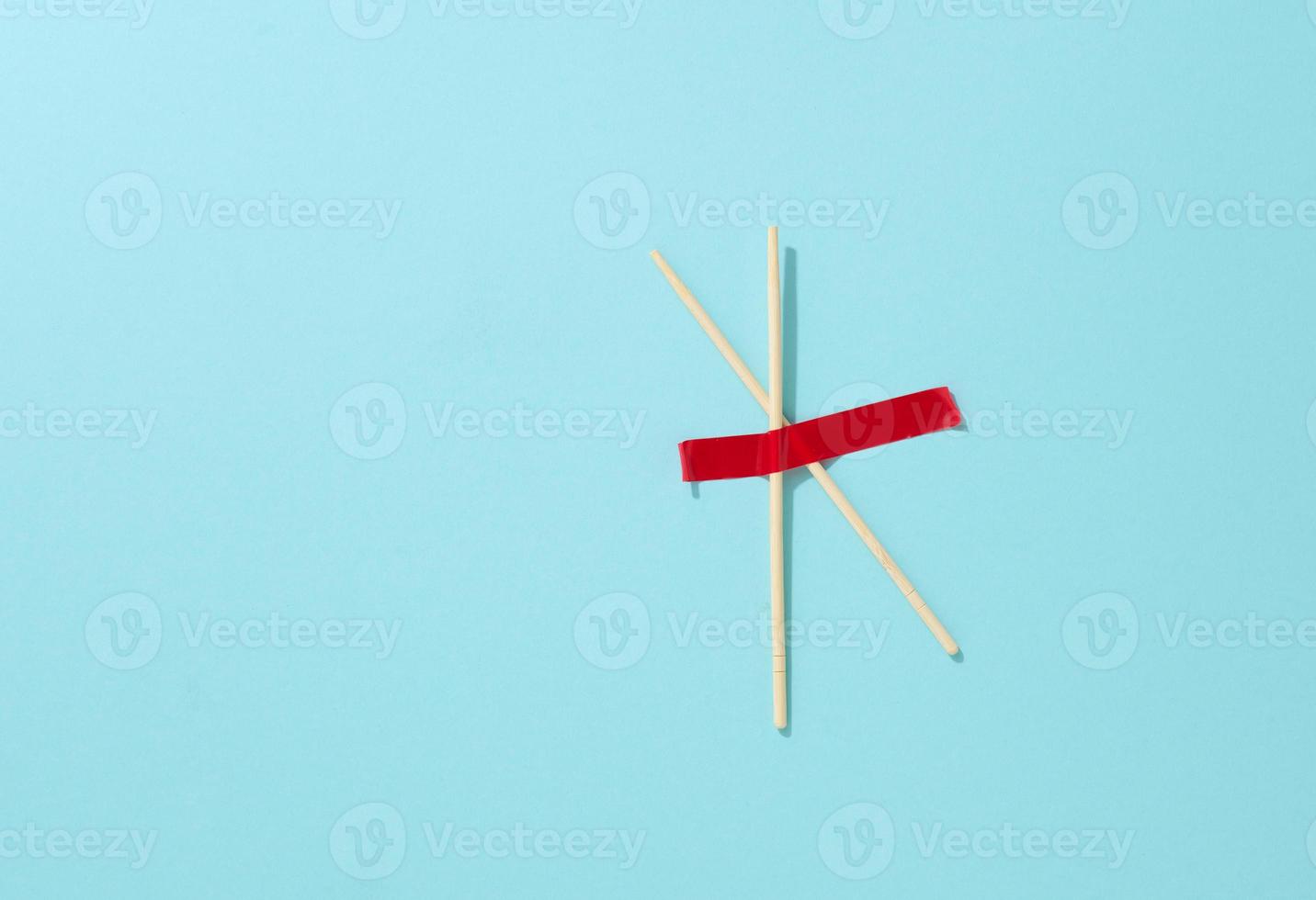 pair of wooden sticks glued with red sticky tape on a blue background, top view photo