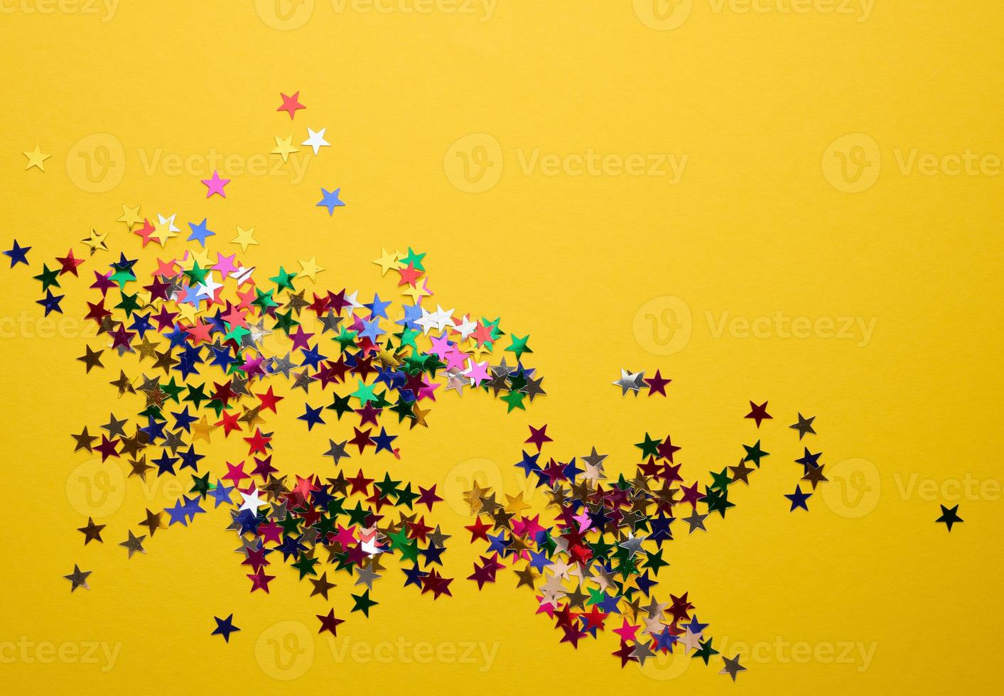 shiny multicolored star confetti scattered on a yellow background, festive backdrop for birthday, valentines day. Festive decoration element photo