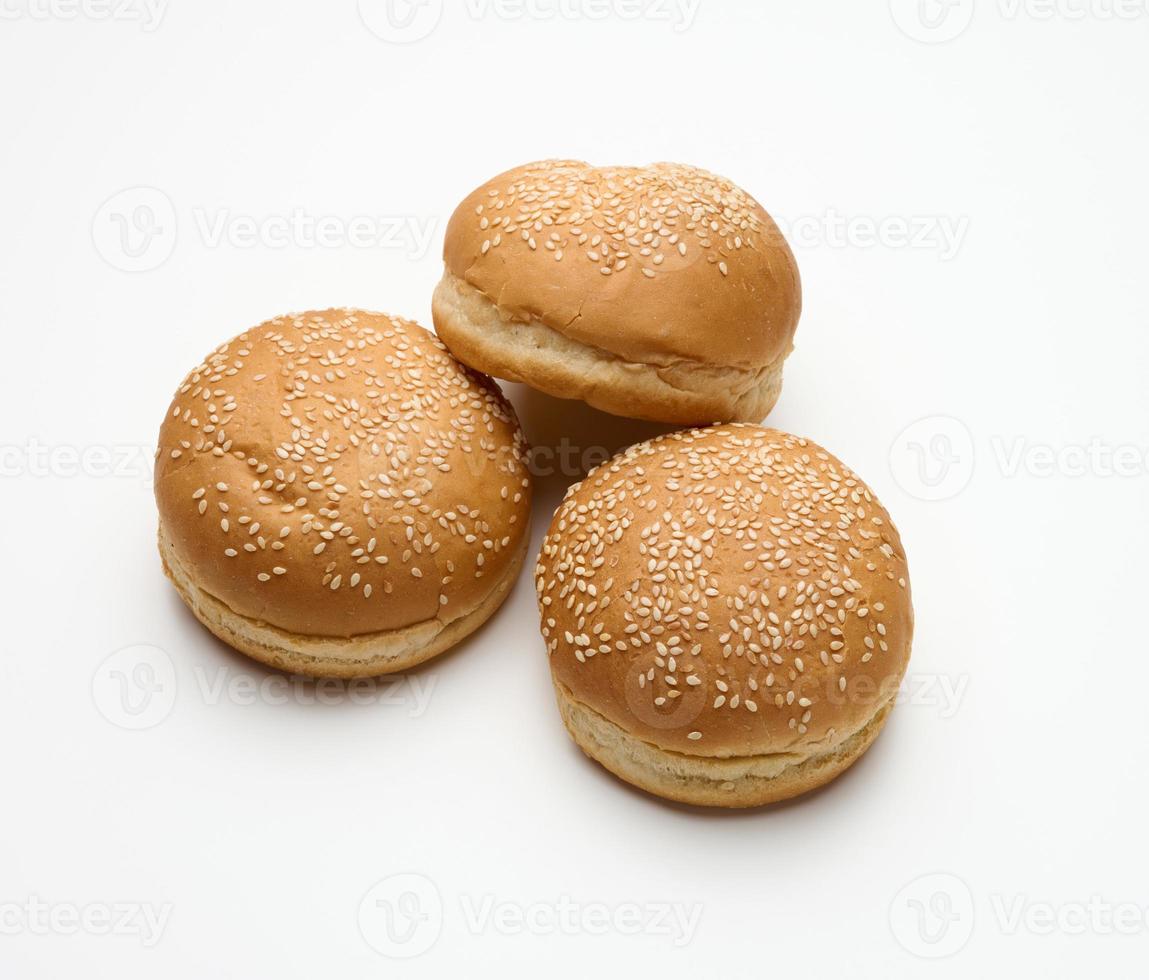 baked round fresh white wheat flour bun sprinkled with sesame seeds on a white table. Hamburger, cheeseberger and sandwich bun photo