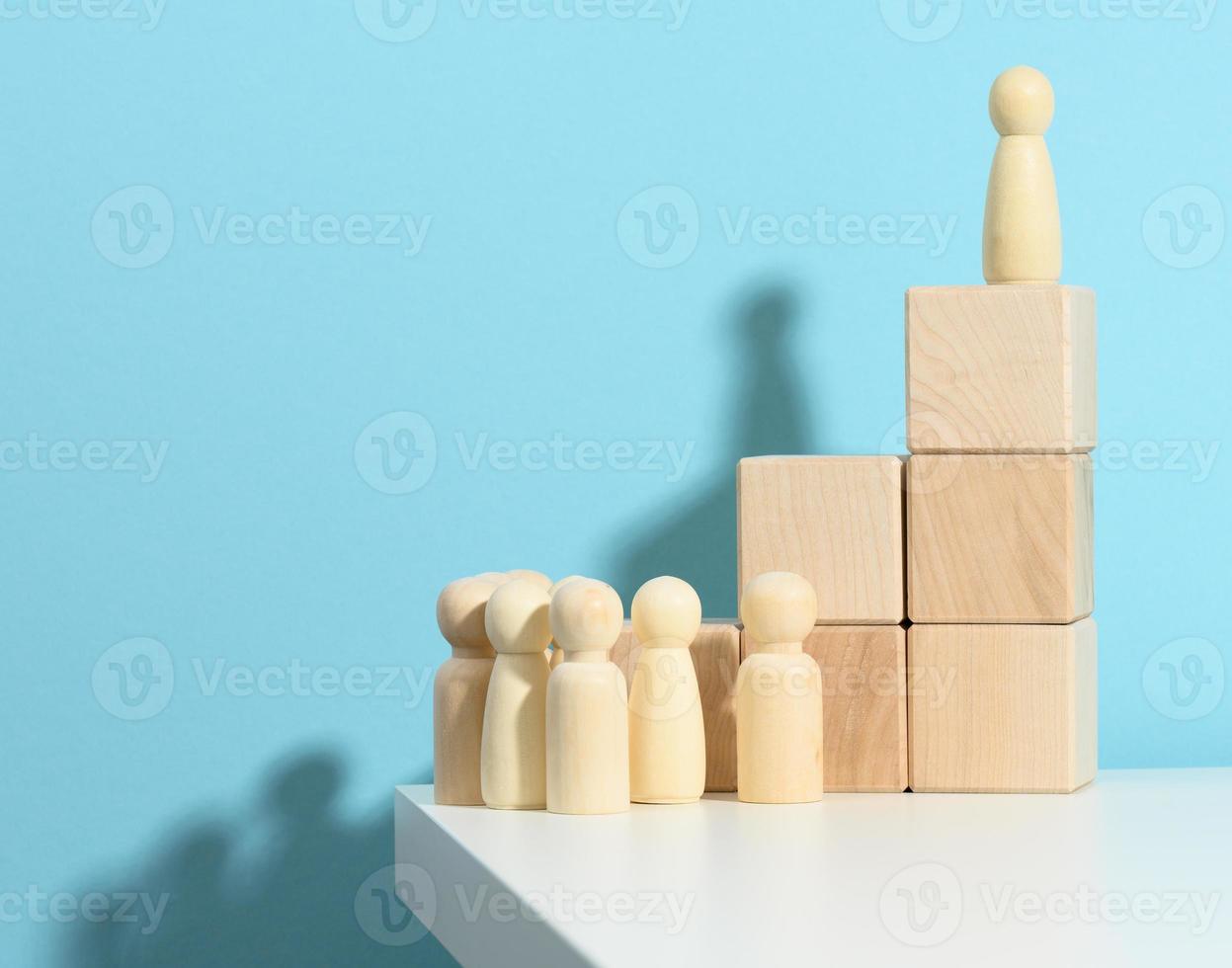 wooden figurine of a man stands on a high podium of cubes, below the crowd. Search for talented employees, rally, manipulation of the masses, selection of employees for the team photo