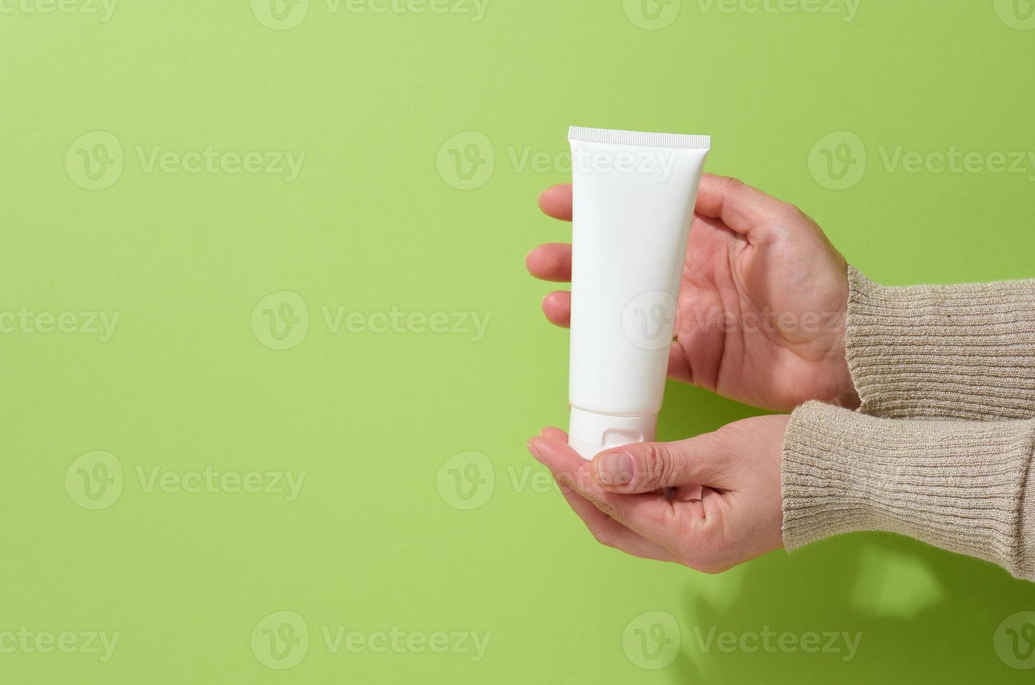 la mano femenina sostiene tubos de plástico blancos vacíos para cosméticos. envases para crema, gel, suero, publicidad y promoción de productos foto