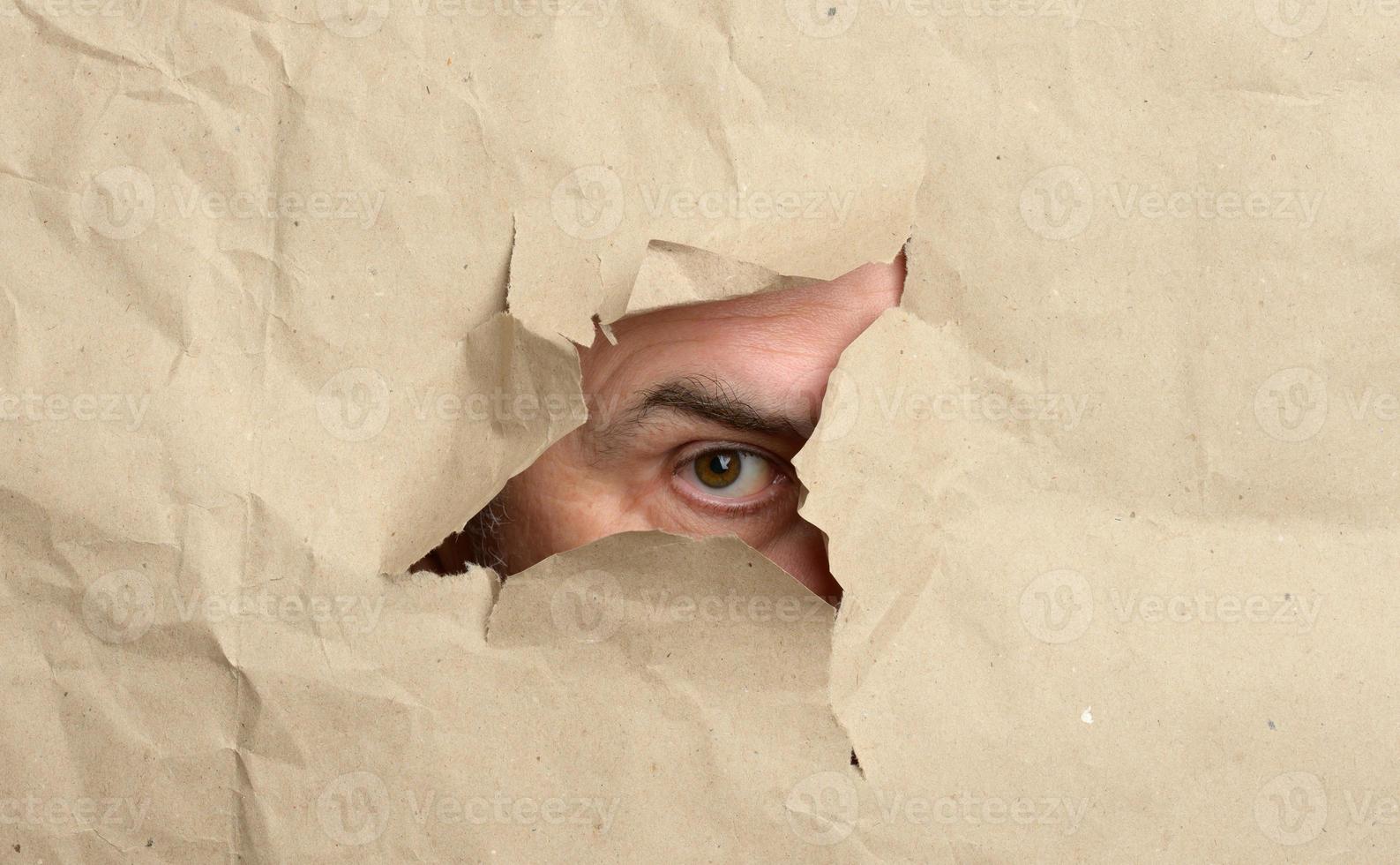 torn hole in brown paper with male peeping eye, man spying and peeping photo