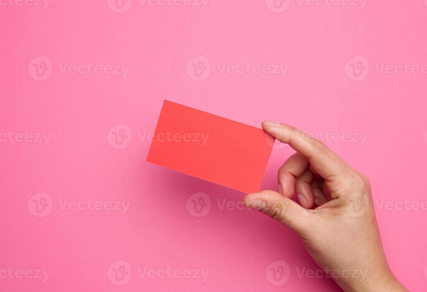 Female hand holding empty  red paper on a pink background. Copy paste image or text photo