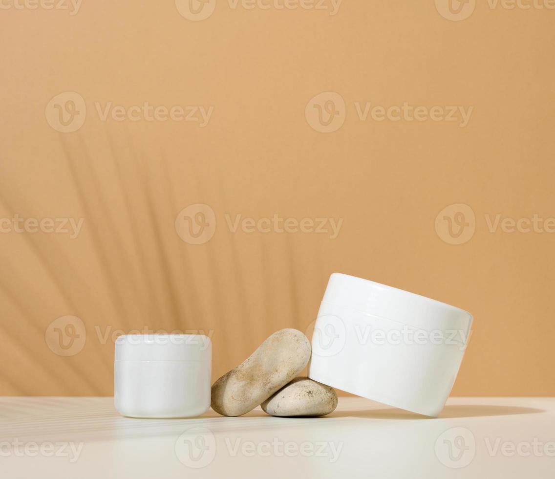 frasco de plástico redondo blanco para productos cosméticos sobre un fondo marrón. sombra de hoja de palma. en blanco para productos de marca, maqueta foto