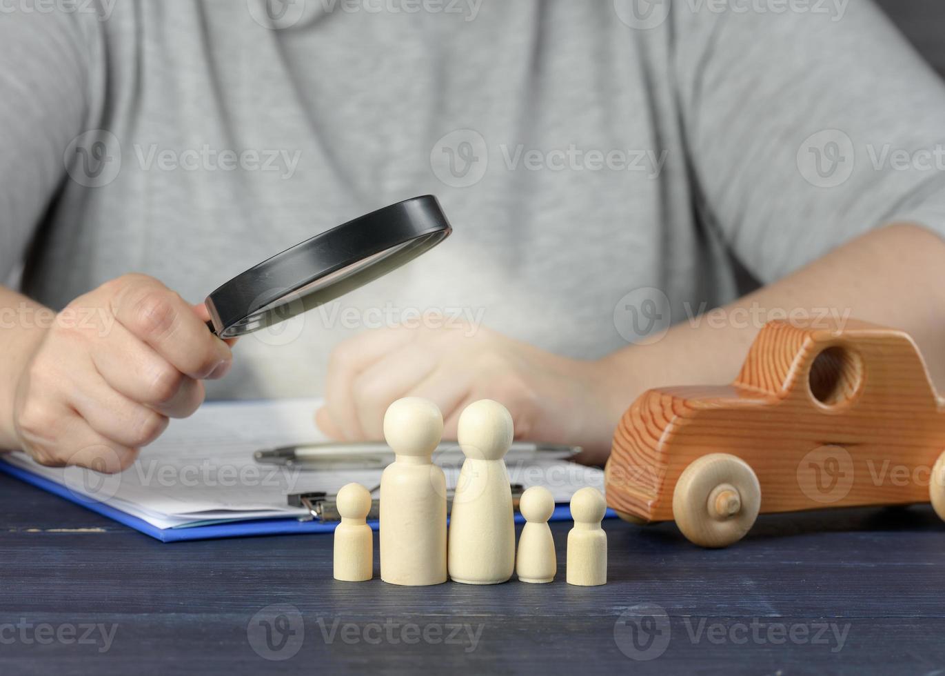 female hand examines wooden figures of the family in a magnifying glass. The concept of studying the credit history of the borrower photo