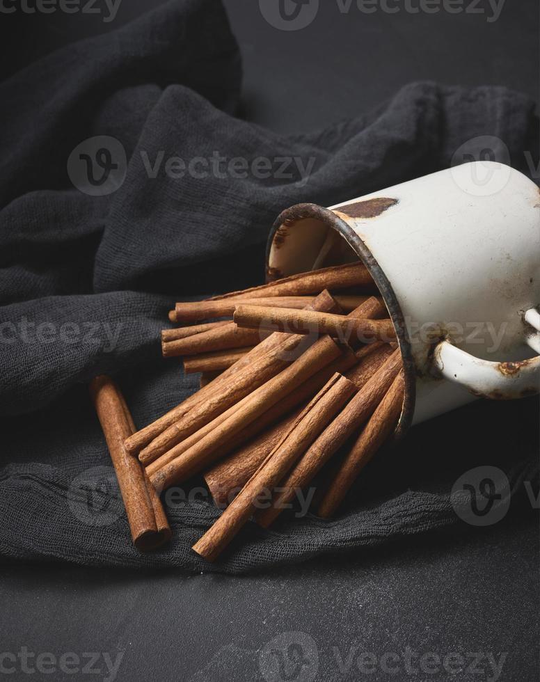 cinnamon sticks in an old metal mug on a black table. Aromatic spice photo