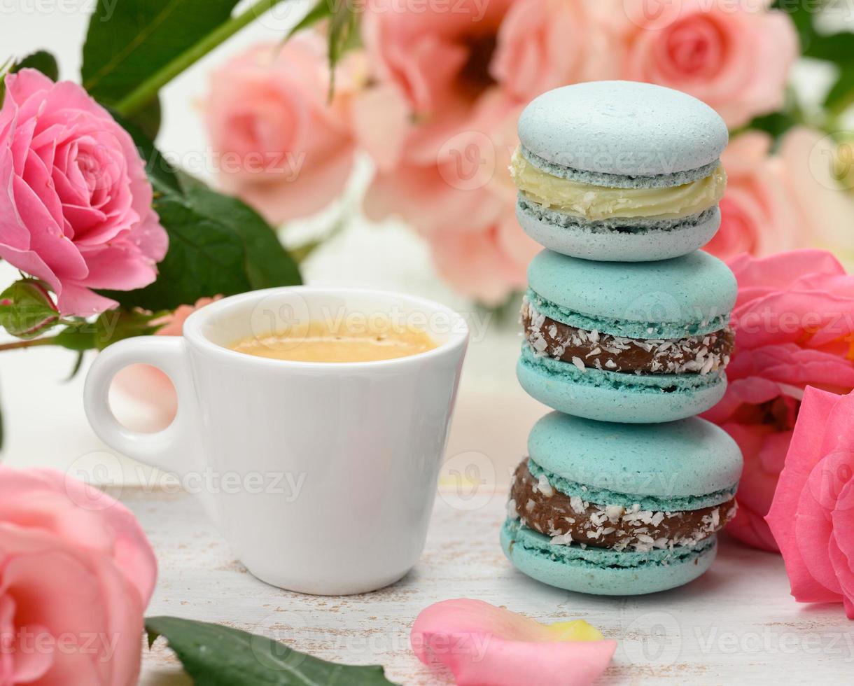 taza de cerámica blanca con café y una pila de macarons azules sobre una mesa blanca foto