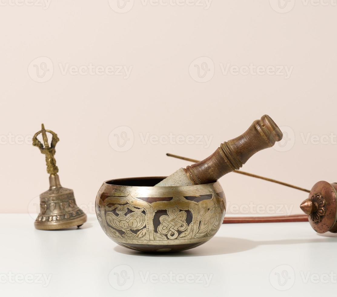 copper singing bowl and wooden clapper on a white table. Musical instrument for meditation, relaxation, various medical practices related to biorhythms, normalization of mental health photo