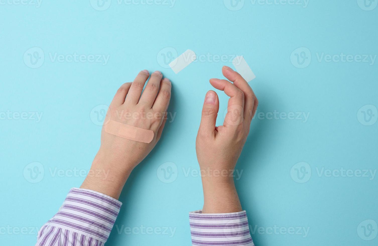 female hand and brown medical adhesive plaster for the treatment of injuries and cuts on the skin, blue background photo