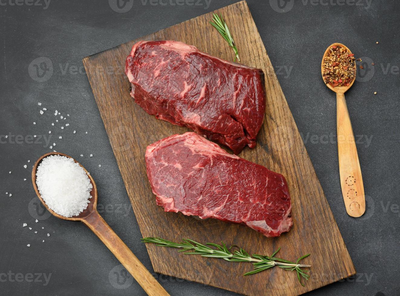 two raw pieces of classic beef steak lie on a wooden board, black table photo