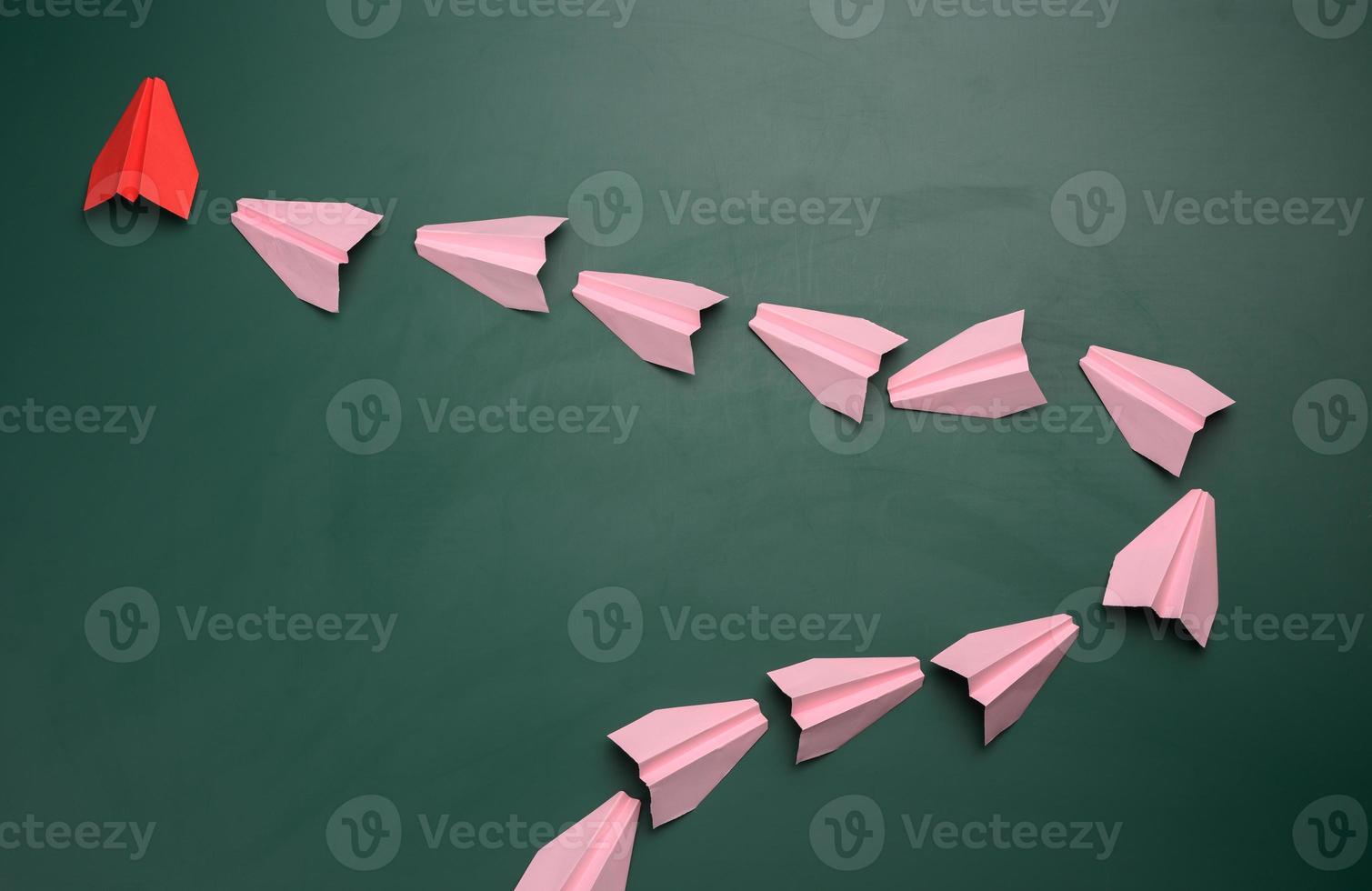 Group of pink paper airplanes following the first red on a green background photo