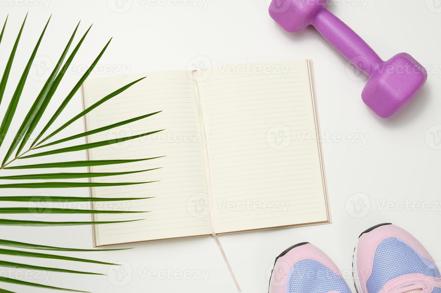 open blank notebook, a pair of sports gym shoes and dumbbells on a white background. Place for recording, top view photo