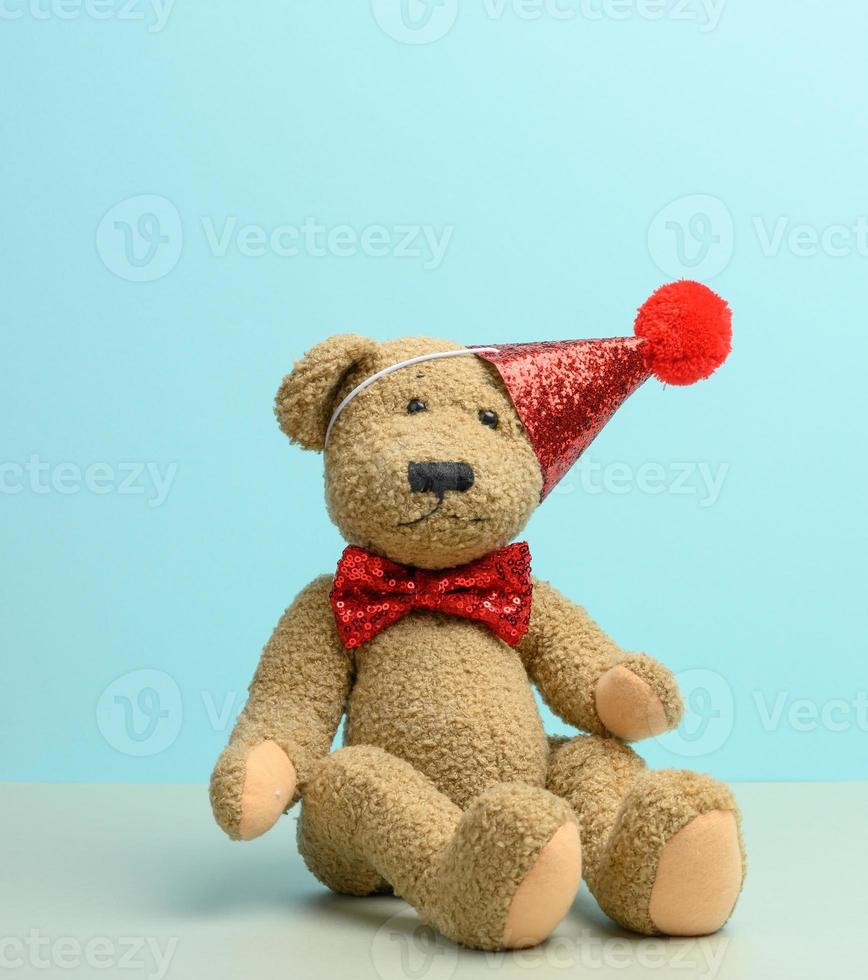 brown teddy bear in a red cap sits on a blue background, photo