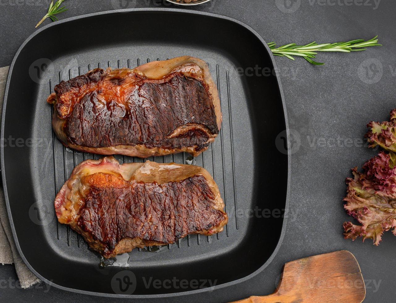 two fried beef pieces are in a frying pan on a black table, degree of readiness of the dish is well don photo