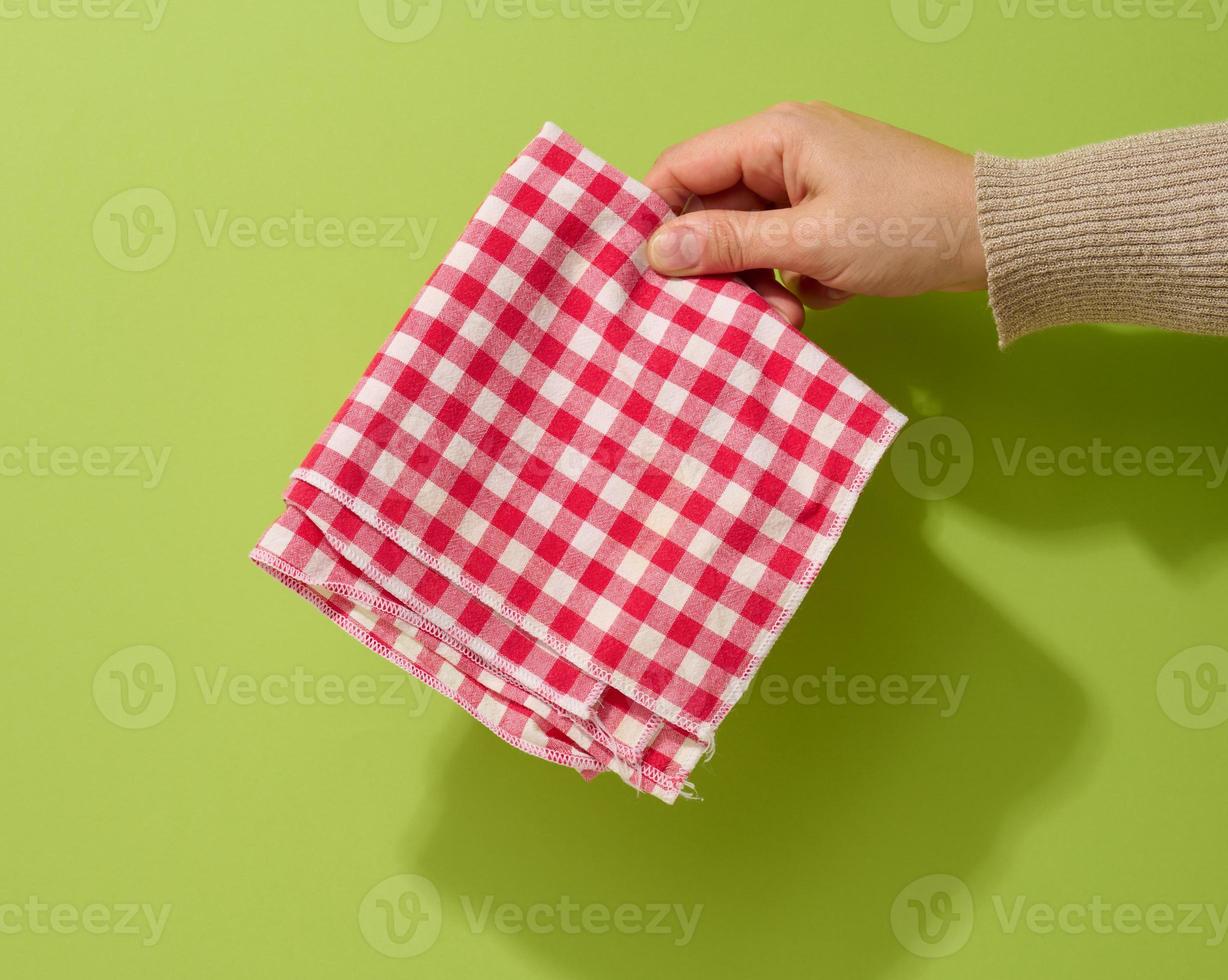 mano femenina sosteniendo una servilleta textil roja-blanca sobre un fondo verde foto