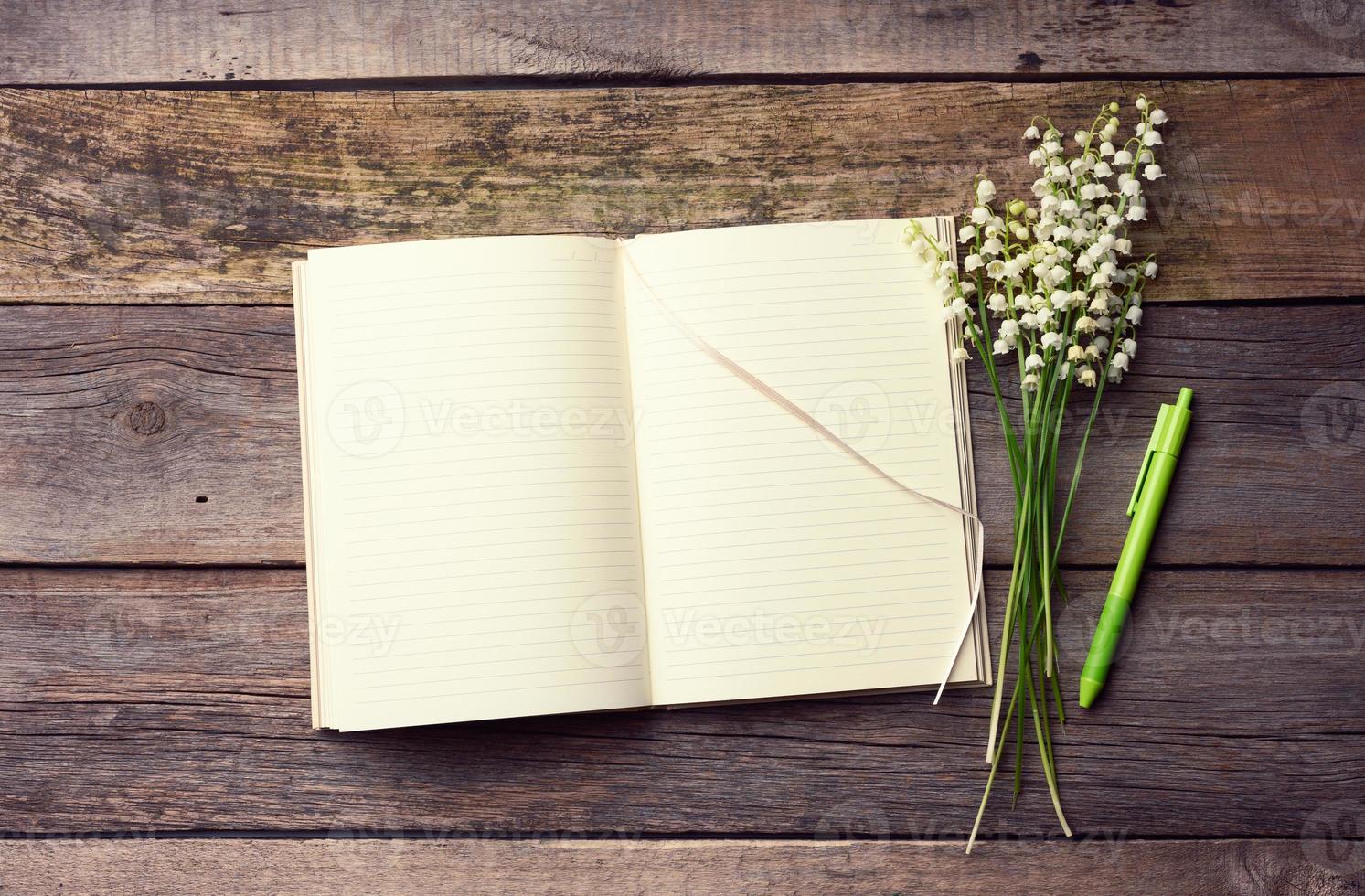 open notebook with blank white sheets and a bouquet of blooming lilies of the valley on a wooden table from gray boards photo
