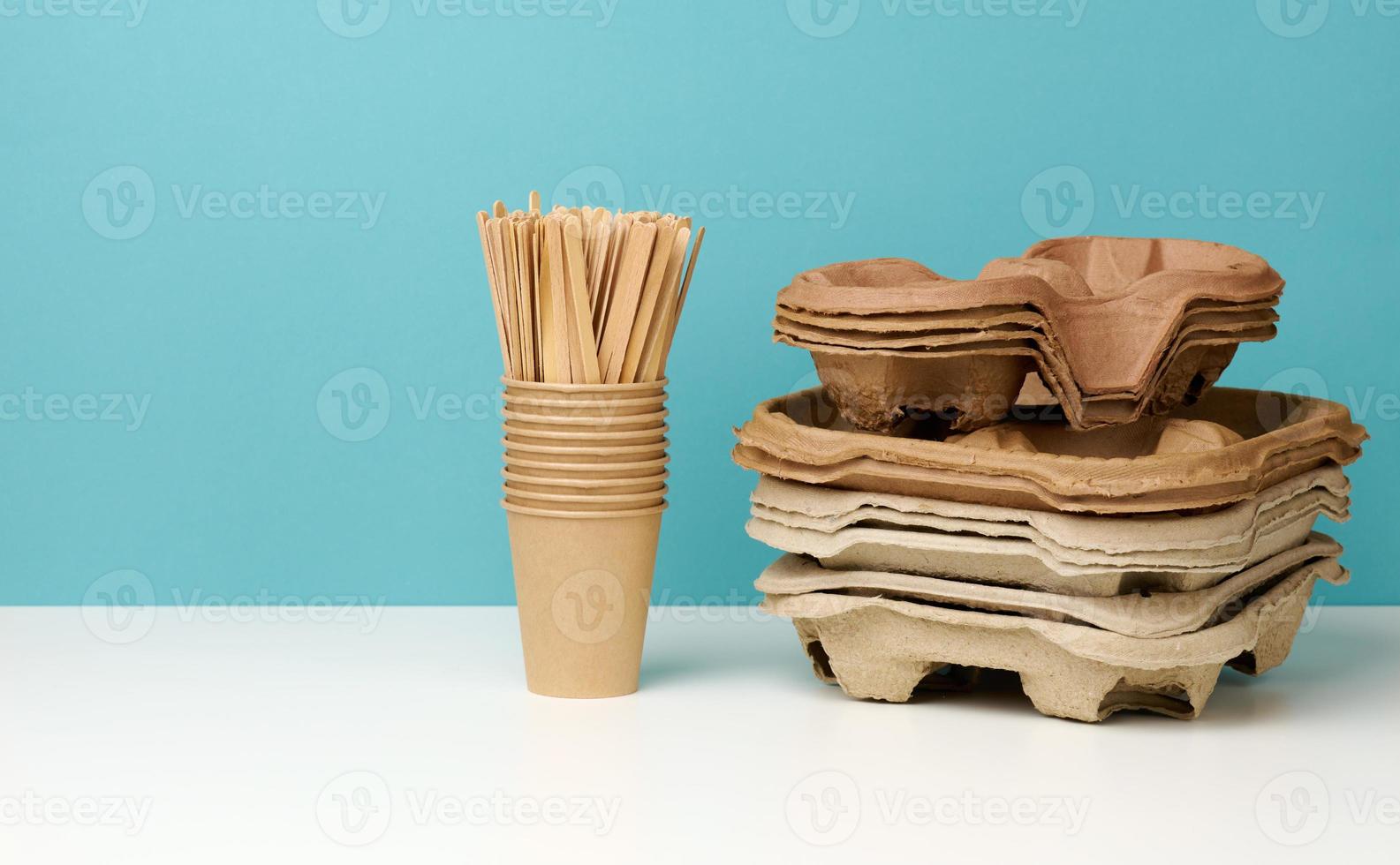 a stack of brown disposable paper cups and a stand on a white table, blue background photo