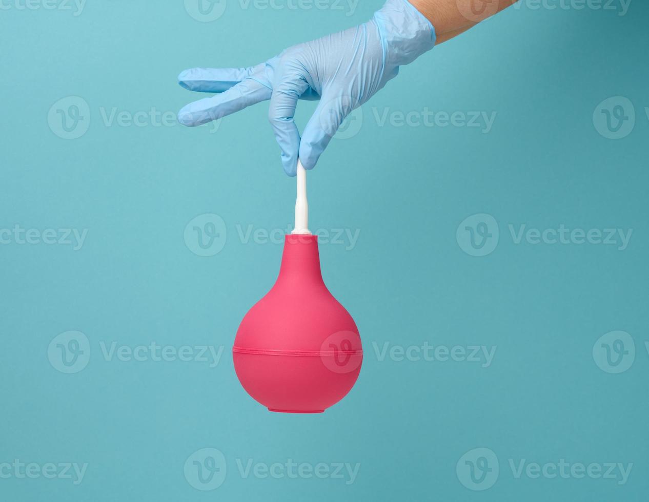 a hand in a blue medical glove holds a pink rubber enema on a blue background photo